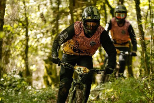 Mountainbiker fährt im Wald und trägt dabei einen Gravity Jersey von DOWE Sportswear in orange-schwarz.