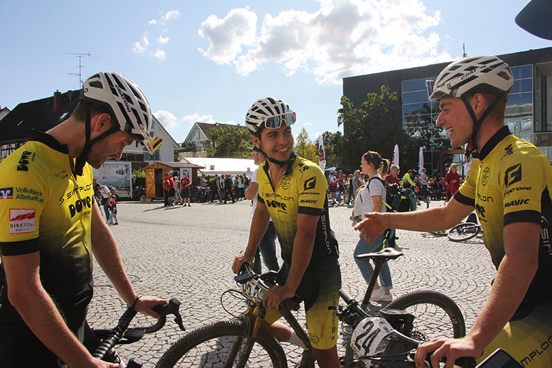 Drei Radler vom Team DOWE Simplon sehen sich lachend an.