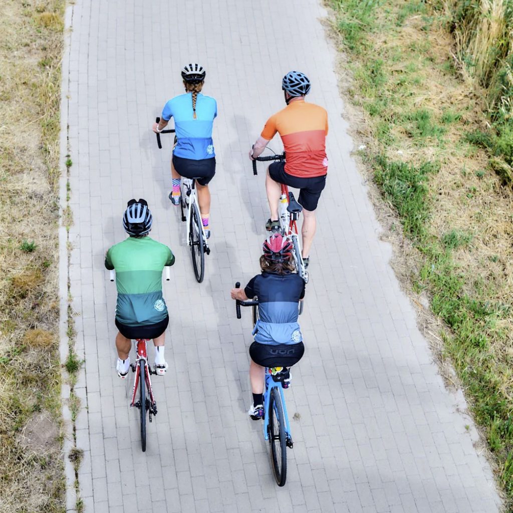 Vier Radfahrer*innen radeln in bunten BasicForm Trikots von DOWE Sportswear