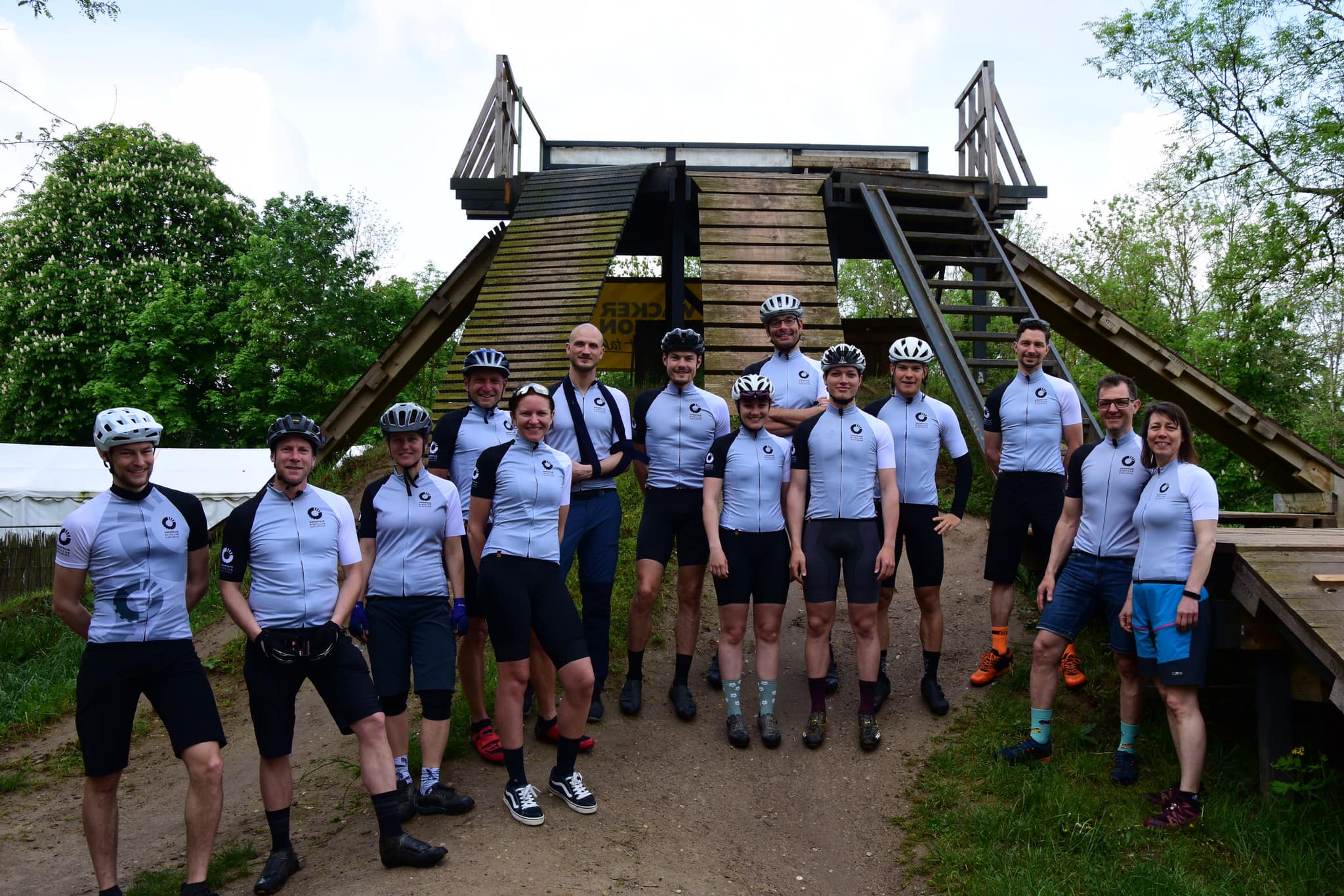 14 Radsportlerinnen in Trikots von DOWE (farbe weiß) vor einer pyramidenförmigen Aussichtsplattform