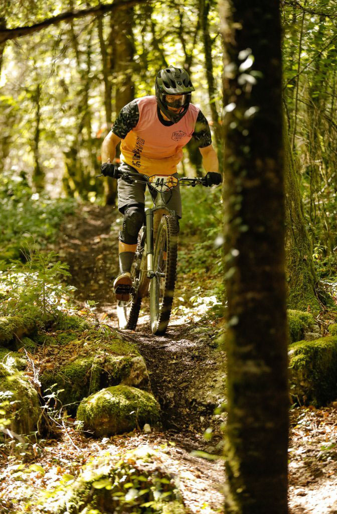 Mountainbiker fährt im Wald und trägt dabei einen Gravity Jersey von DOWE Sportswear in orange-schwarz.