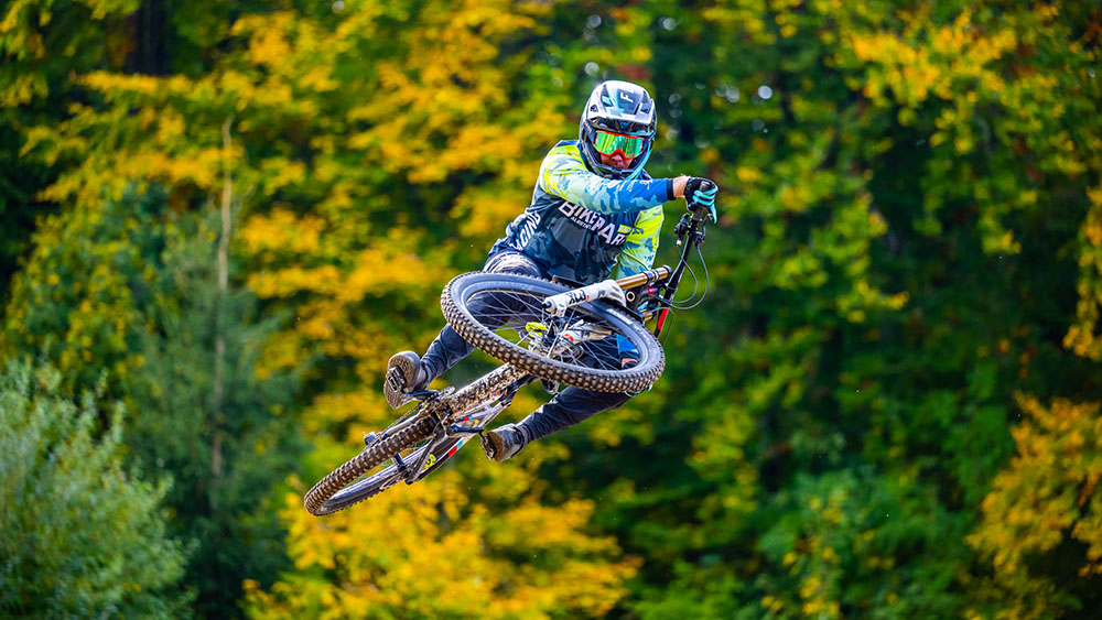 DOWE Sportswear Gravity Jersey, getragen von Mountainbiker des BikePark Albstadt - Grün-Blaues Camo-Muster - MTB-Radler springt