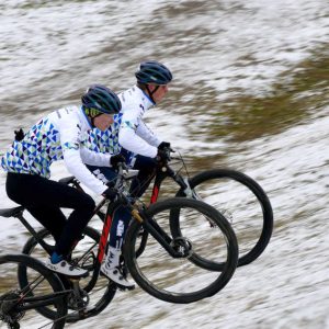 Kreativ: Zwei KTM-Youngsters im DOWE-Trikot radeln auf ihren Mountainbikes einen beschneiten Hügel aufwärts. Sie tragen auch Helme.